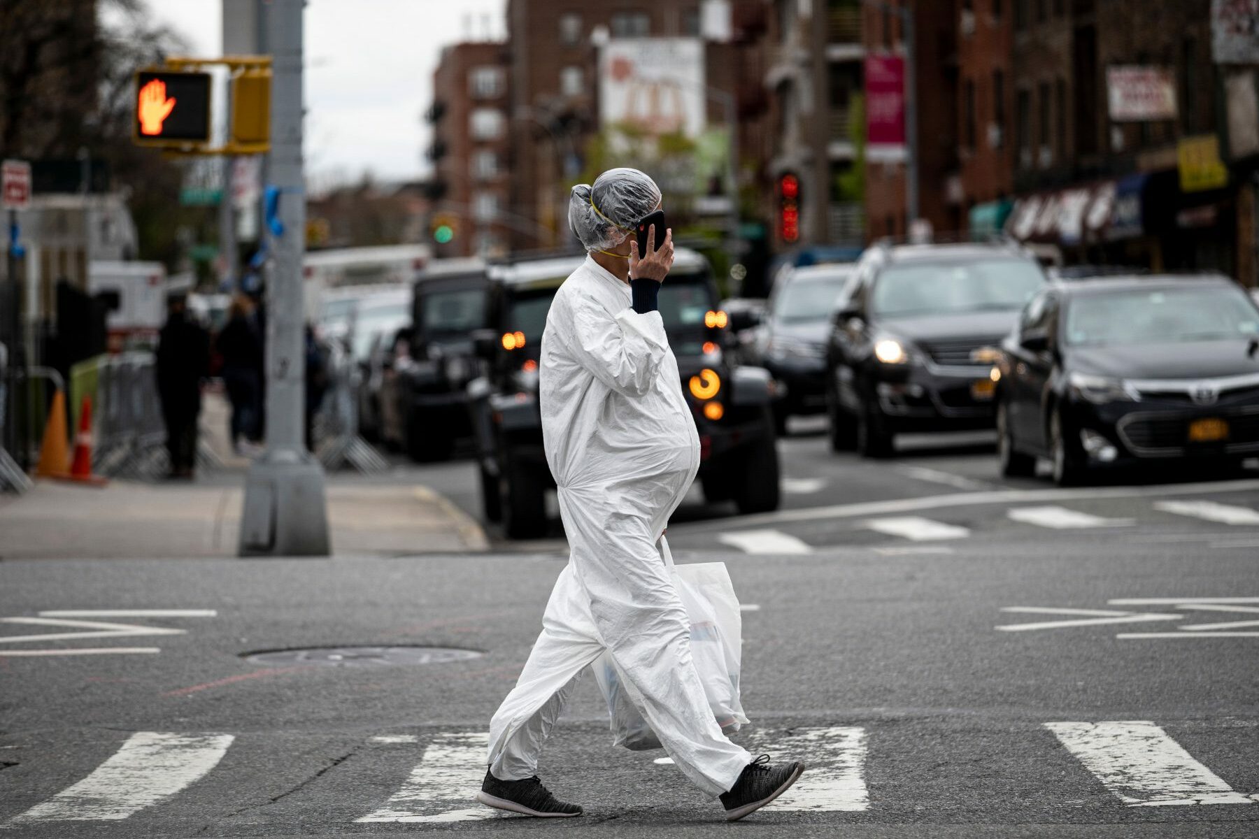 A pregnant woman wearing a hazmat suit and a mask walks in the streets.