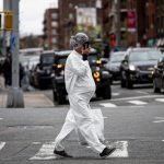A pregnant woman wearing a hazmat suit and a mask walks in the streets.