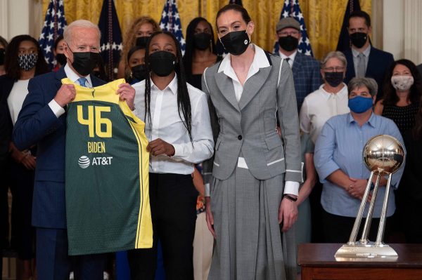 President Biden holding a basketball jersey standing by members of the Seattle Storm.