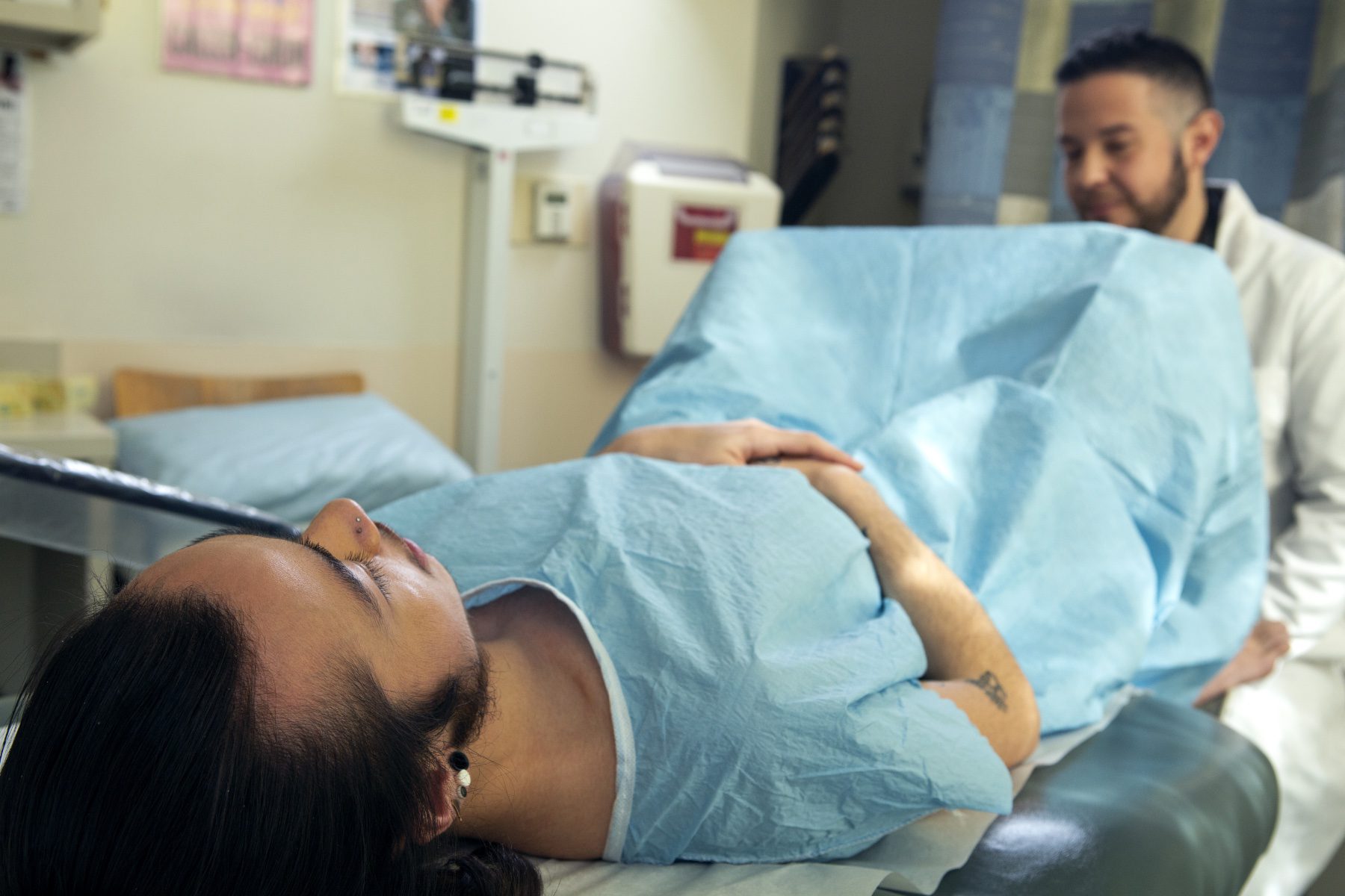 A genderqueer person in a hospital gown receiving a pelvic exam.