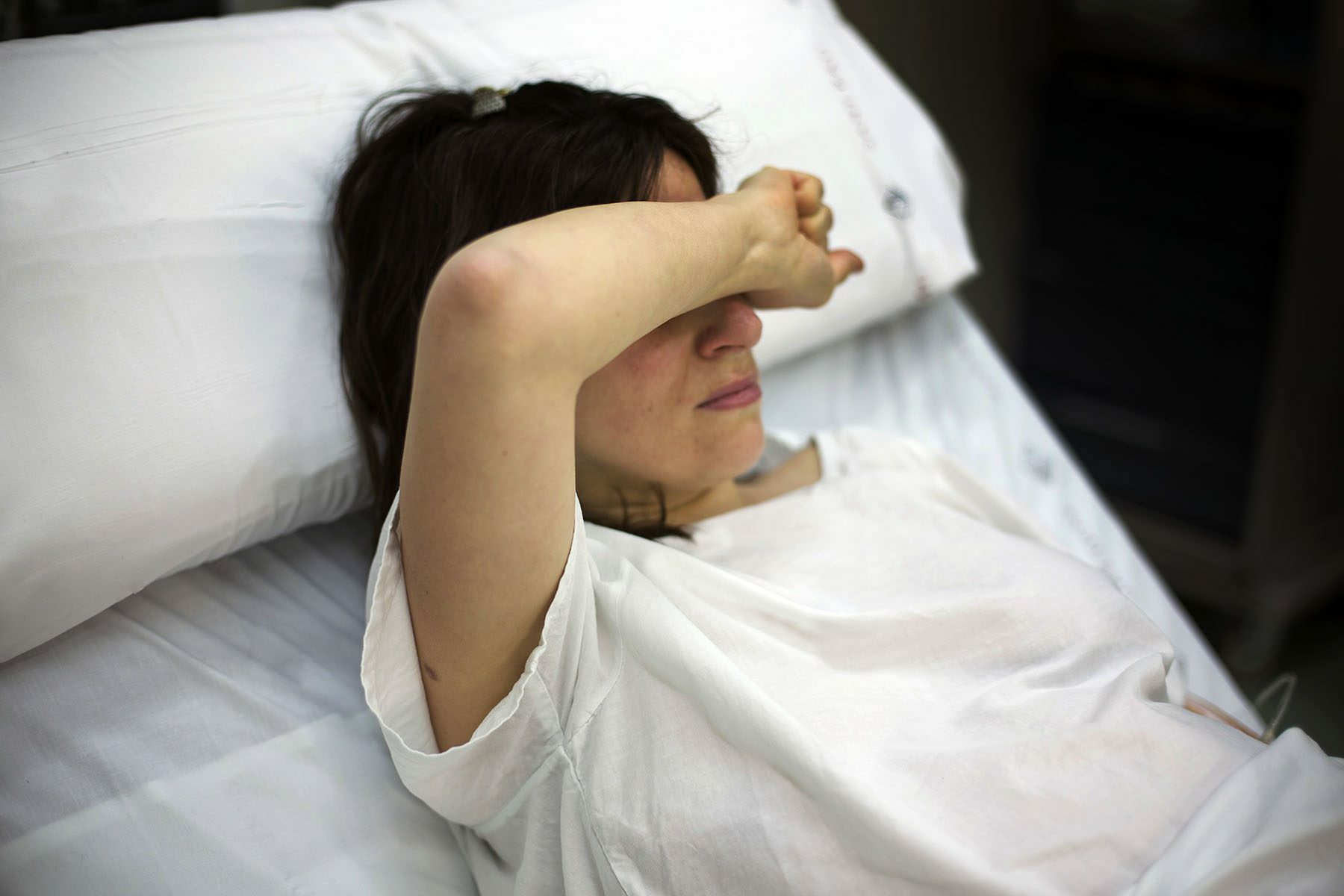 A pregnant woman covers her face while lying in a hospital bed.