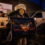 A black woman holds a sign with a picture of R. Kelly with the word #MuteRKelly printed over his face during a demonstration in support of the singer's victims.