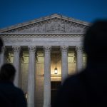 Shadowy figures are seem standing in front of the U.S. Supreme court.