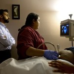 A doctor and a sonographer perform a sonogram on a pregnant patient inside an examination room.