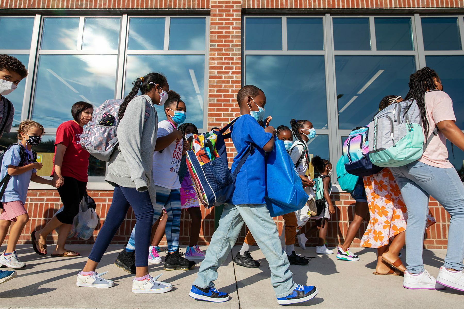 Young students wearing face masks prepare to enter their elementary school on the first day of classes.