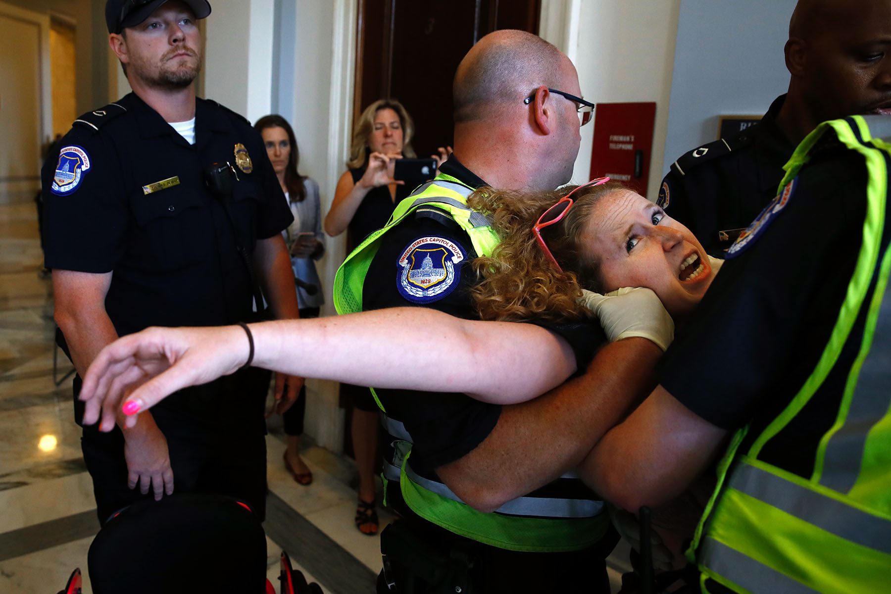 A woman is being carried by multiple capitol police officers. She seems to be struggling greatly.