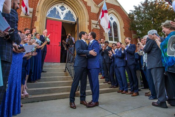 Pete Buttigieg and Chasten Glezman kiss in front of a cathedral while wedding-goers smile and clap.