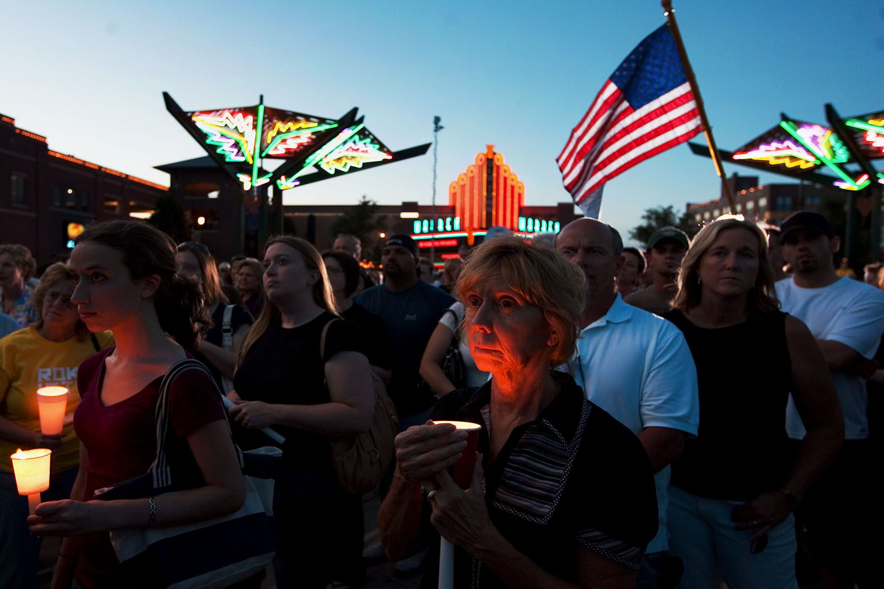 People participate in a candlelight vigil. They have solemn expressions.