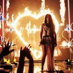 Kacey Musgraves is seen on stage surrounded by impressive pyrotechnics including neon heart shaped props and a heart on fire.