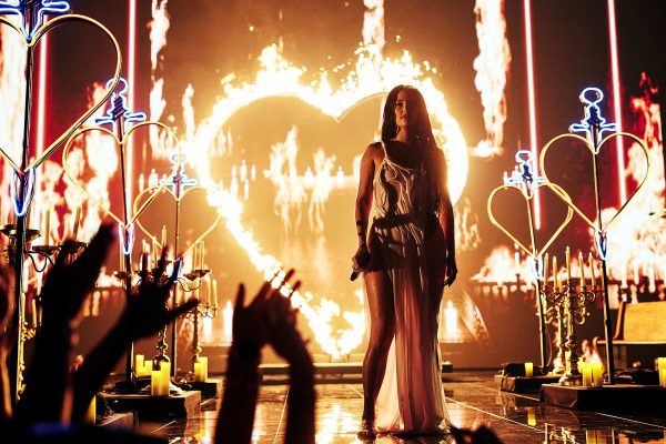 Kacey Musgraves is seen on stage surrounded by impressive pyrotechnics including neon heart shaped props and a heart on fire.