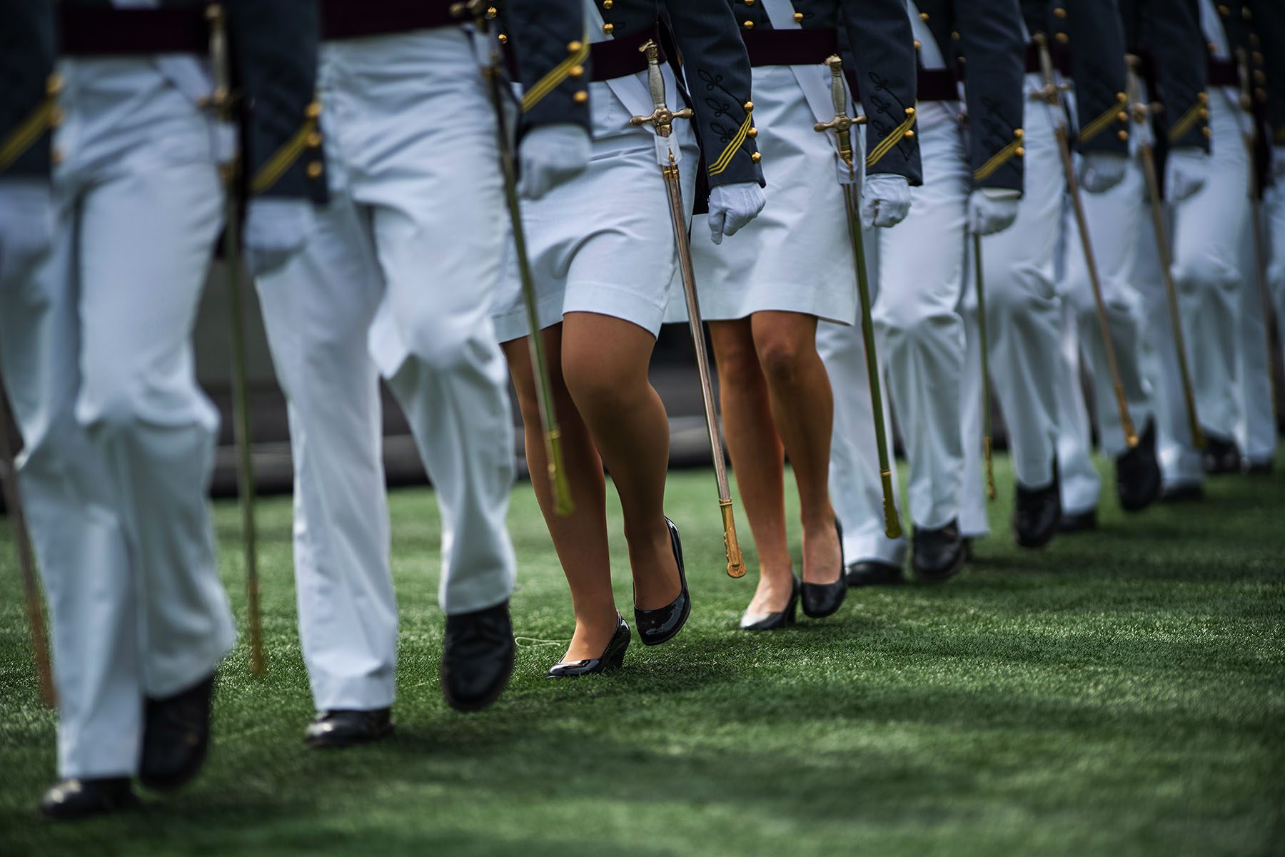 Military Academy cadets, some wearing skirts and pumps, some wearing pants, march to their graduation ceremony.