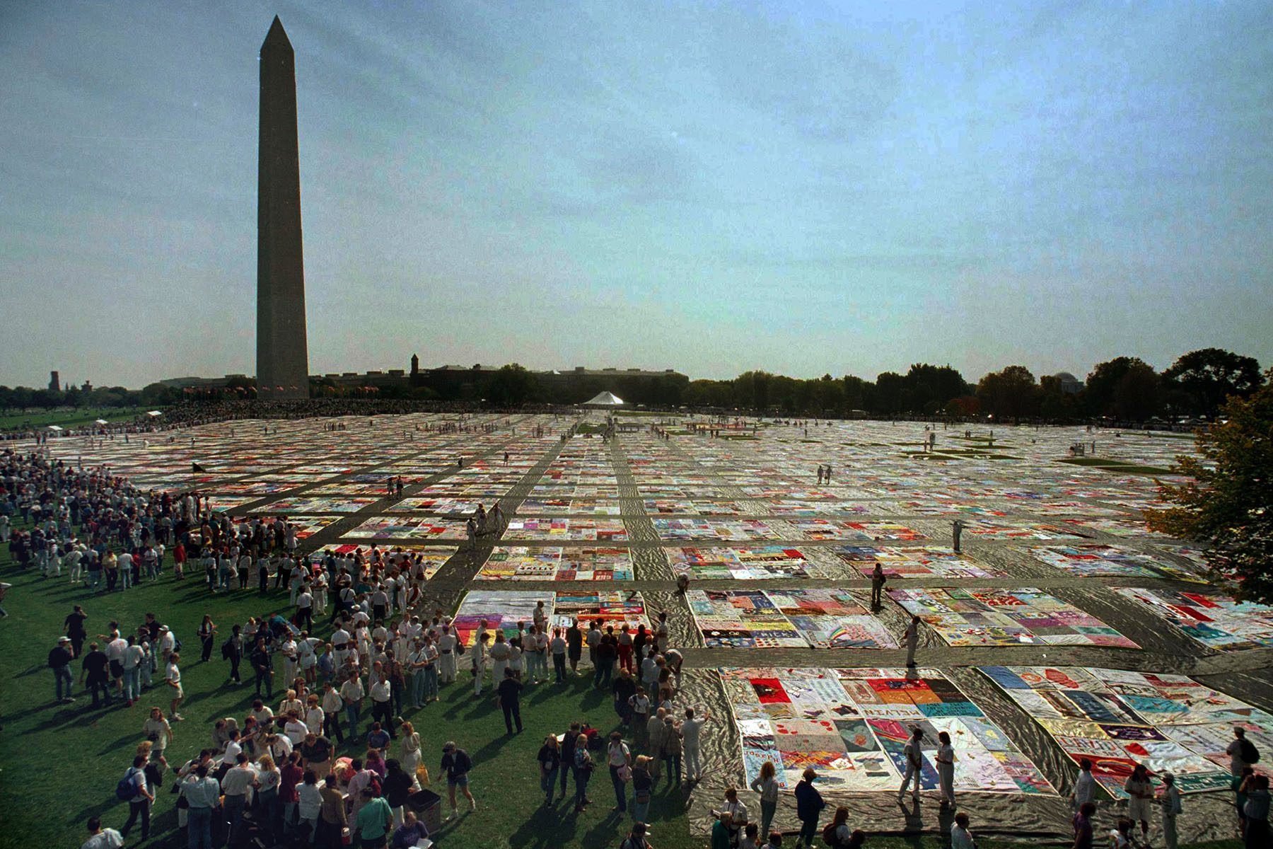 A view of the Washington Monuments captures a massive patchwork laid all around the lawn while crowds look at the patchwork.