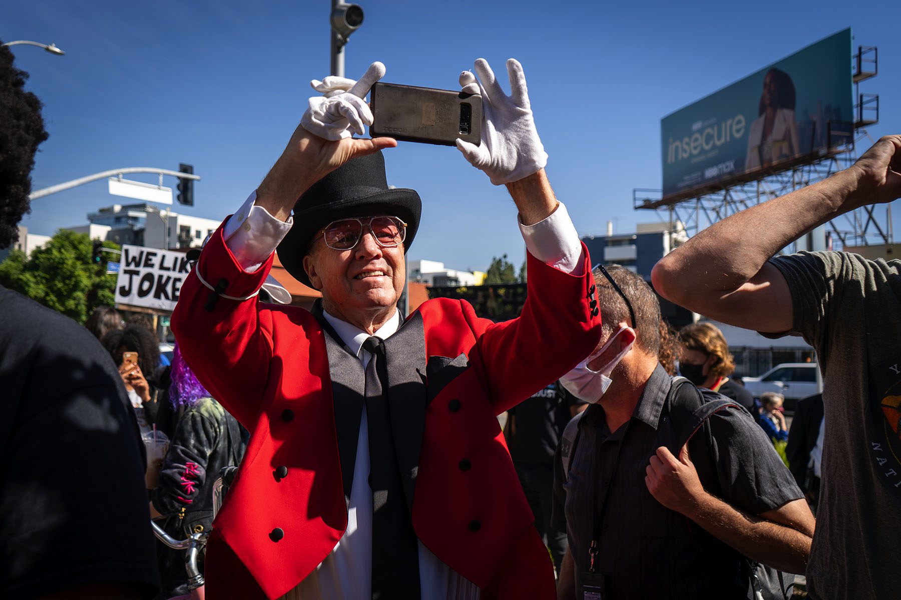 A participant wearing a red suit, a top hat and white gloves takes a photo on their phone.