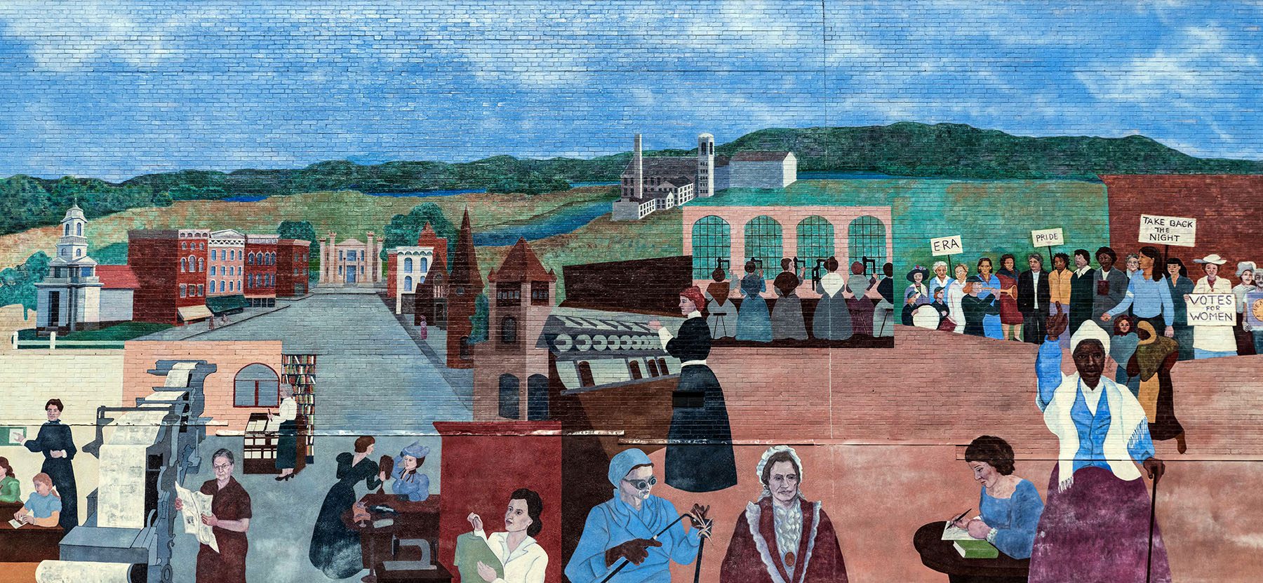 A mural depicts the town of Northampton. All around the town are women; some paint, write, read and others hold signs in protest.