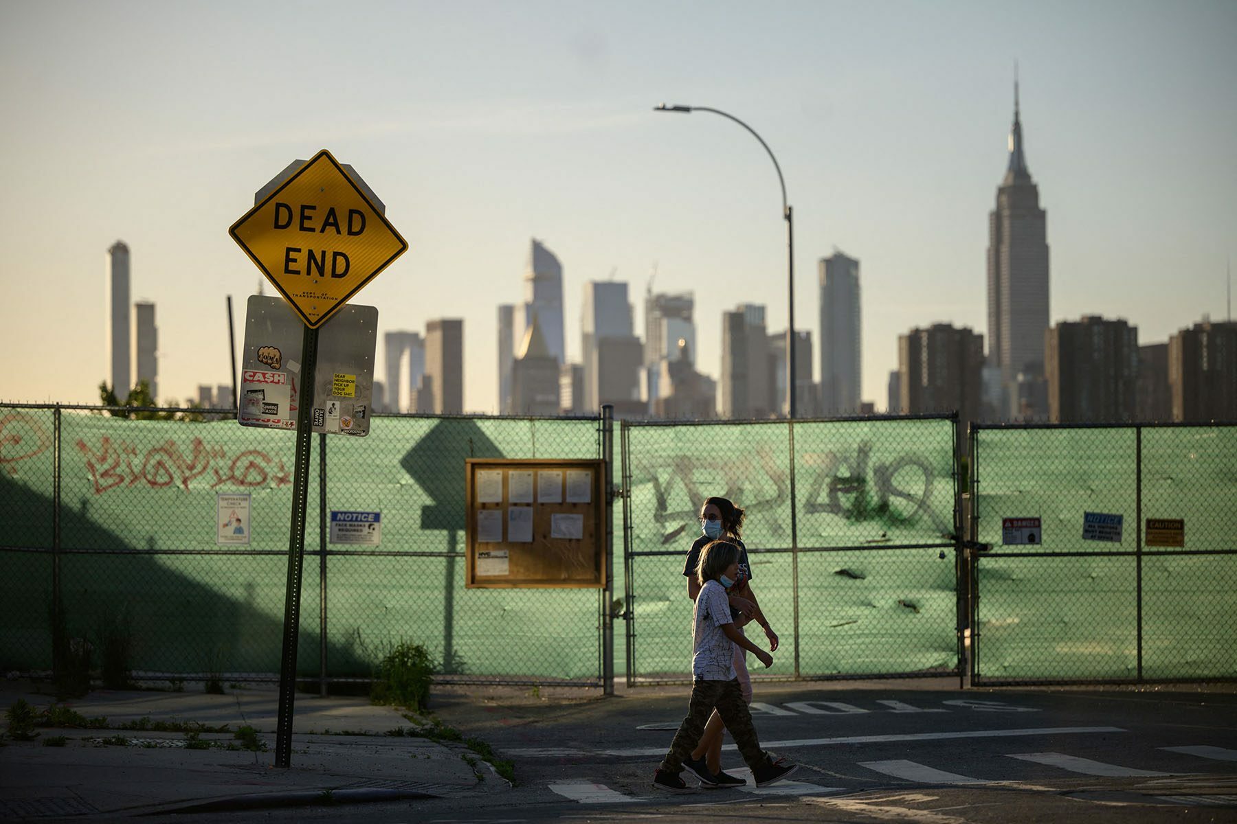 Pedestrians pass a 'dead end' sign before the Manhattan city skyline.