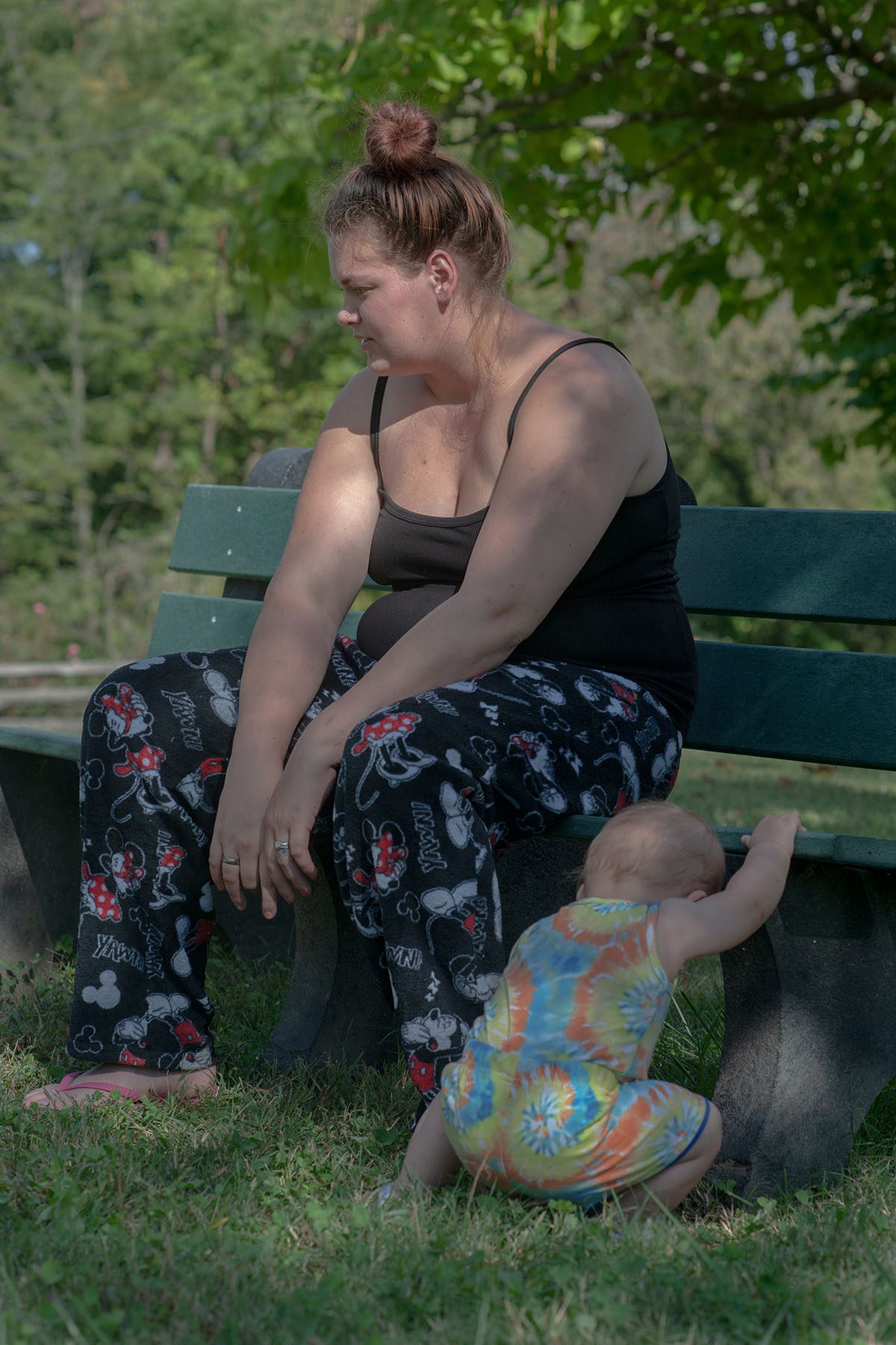 Desiree Abott sit on a bench as her youngest son plays in the grass.