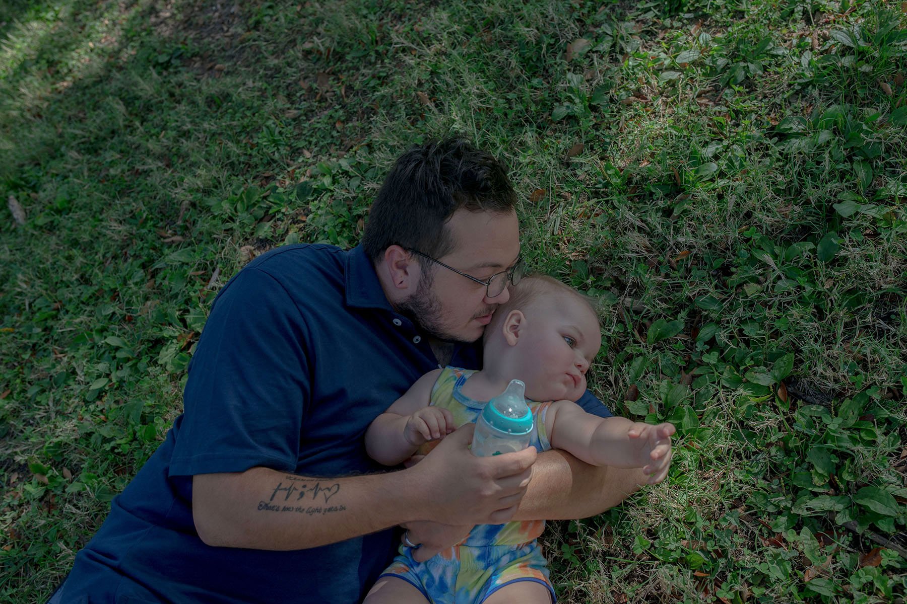 Steven Bryant plays with his son in the grass while holding a baby bottle.