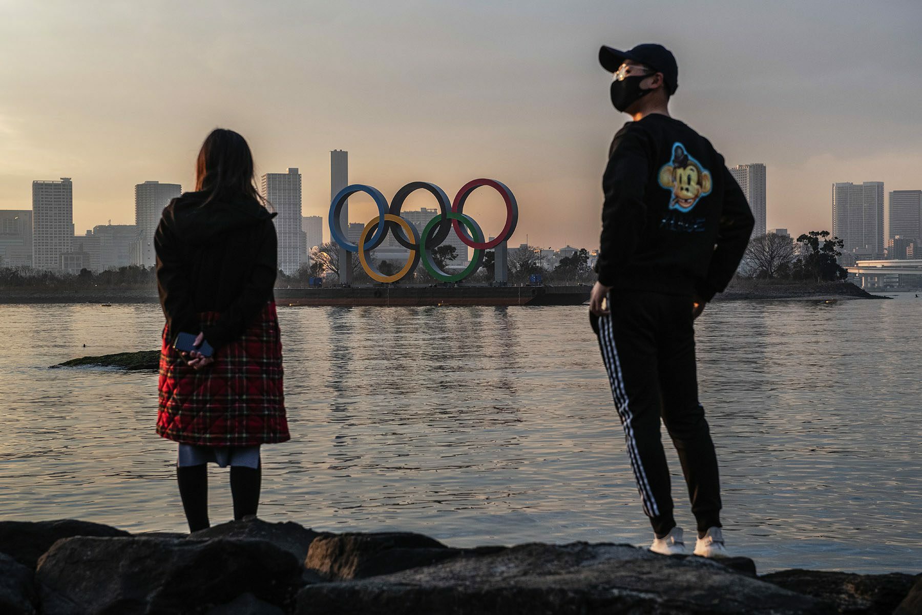 People strand by the water looking at the Olympic Rings in Tokyo.