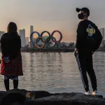 People strand by the water looking at the Olympic Rings in Tokyo.