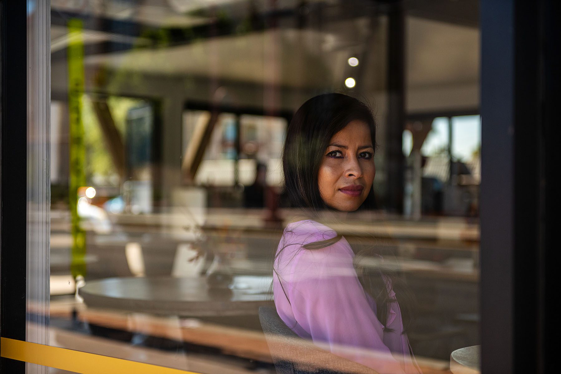 Ylenia Aguilar looks out the window as she poses for a portrait in a cafe