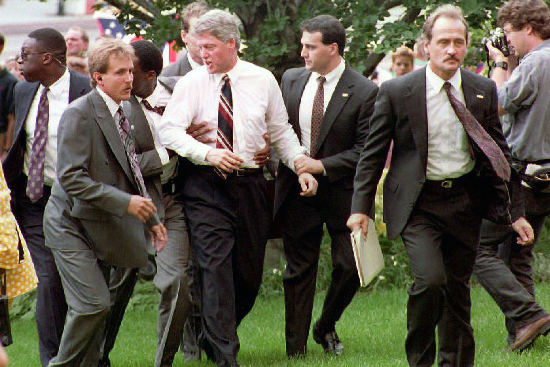 Bill Clinton is surrounded by secret service as they move him away from a crowd.