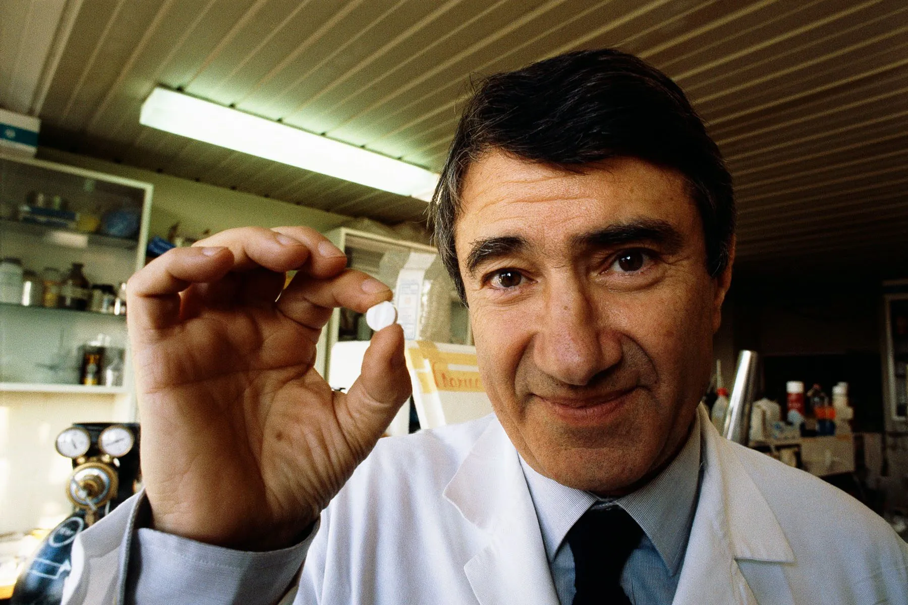 Professor Etienne-Emile Baulieu poses in a lab with a pill in his hand.
