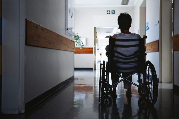 A senior woman sits in a wheelchair inside an assisted living facility.
