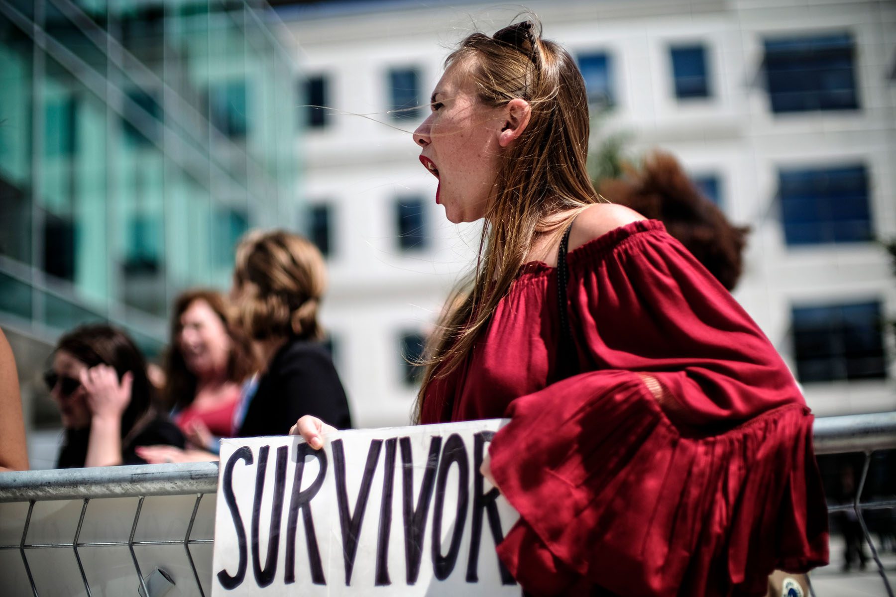 A woman is seen holding a sign that reads "survivor" and chanting slogans at a gathering.