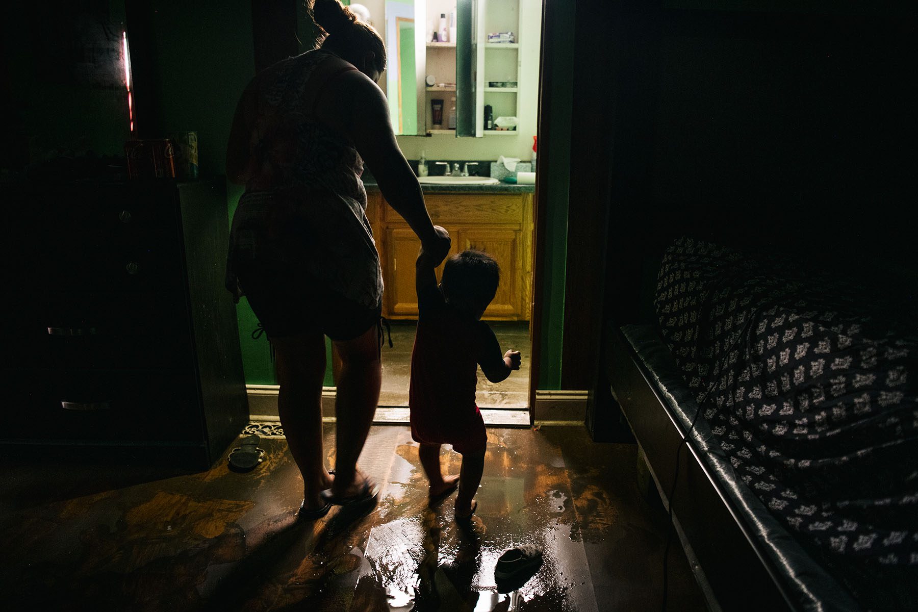 A woman holds a toddler as they walk through a flooded home.