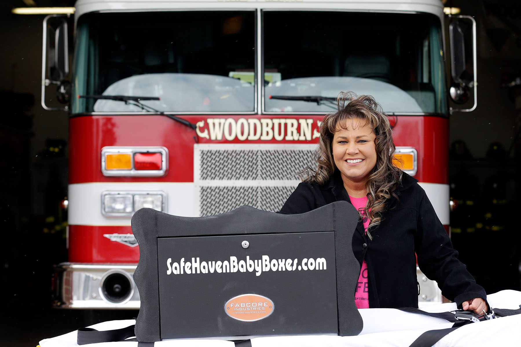 Monica Kelsey poses with a baby box in front of a firetruck.