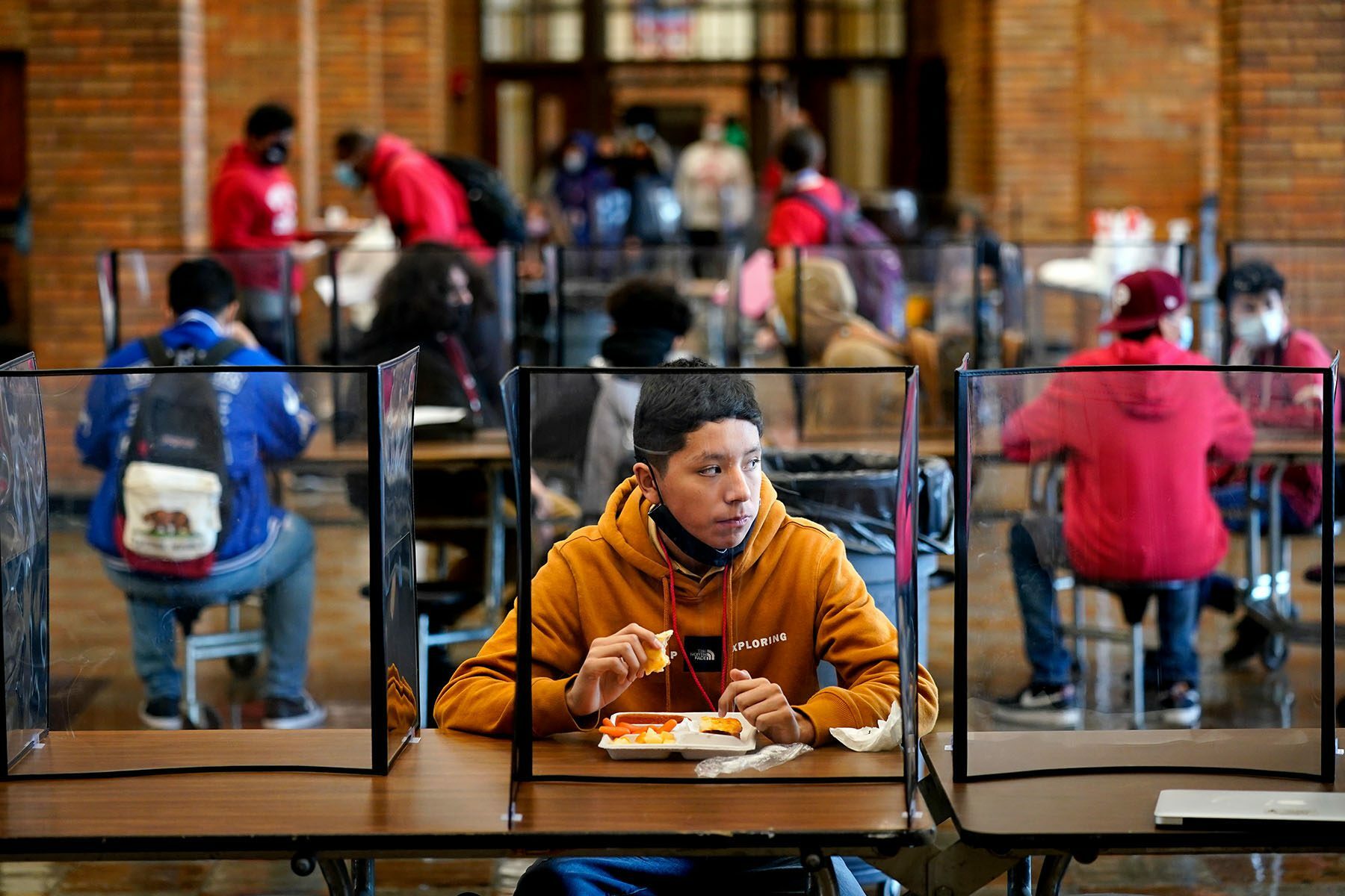 Students eat lunch separated from classmates by plastic dividers.