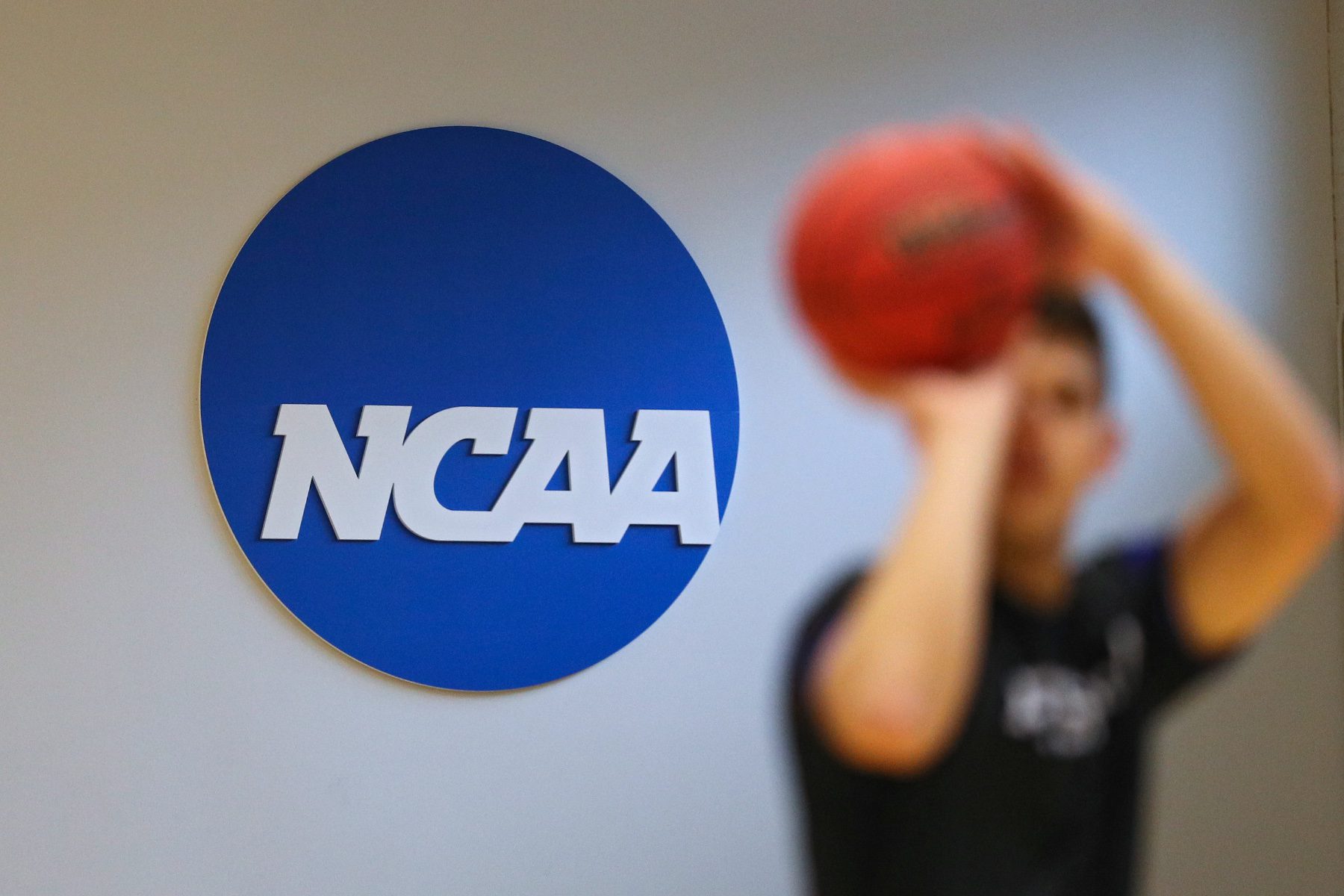 A person prepares to shoot a basketball standing in front of a NCAA logo.