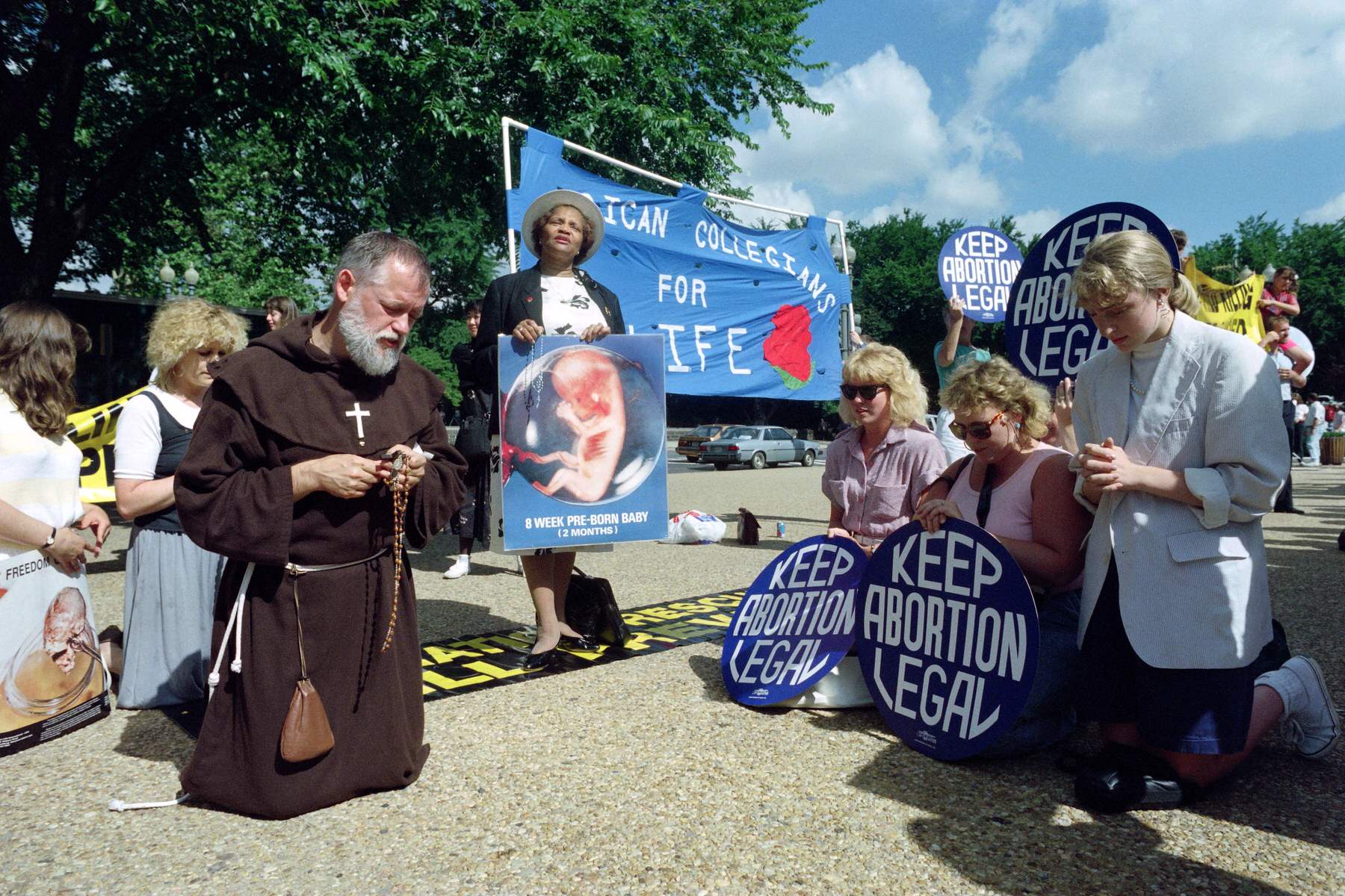 A priest kneels across from abortion rights demonstrators in Washington in 1989