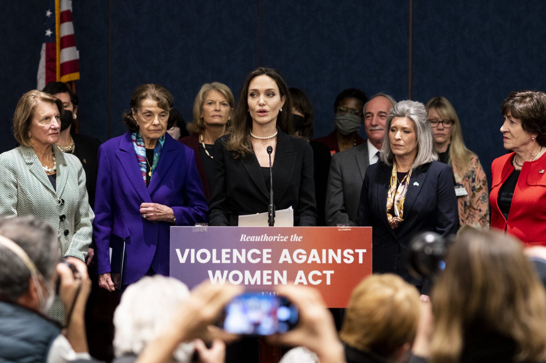 Angelina Jolie stands with women senators at a lectern that says "Violence Against Women Act"