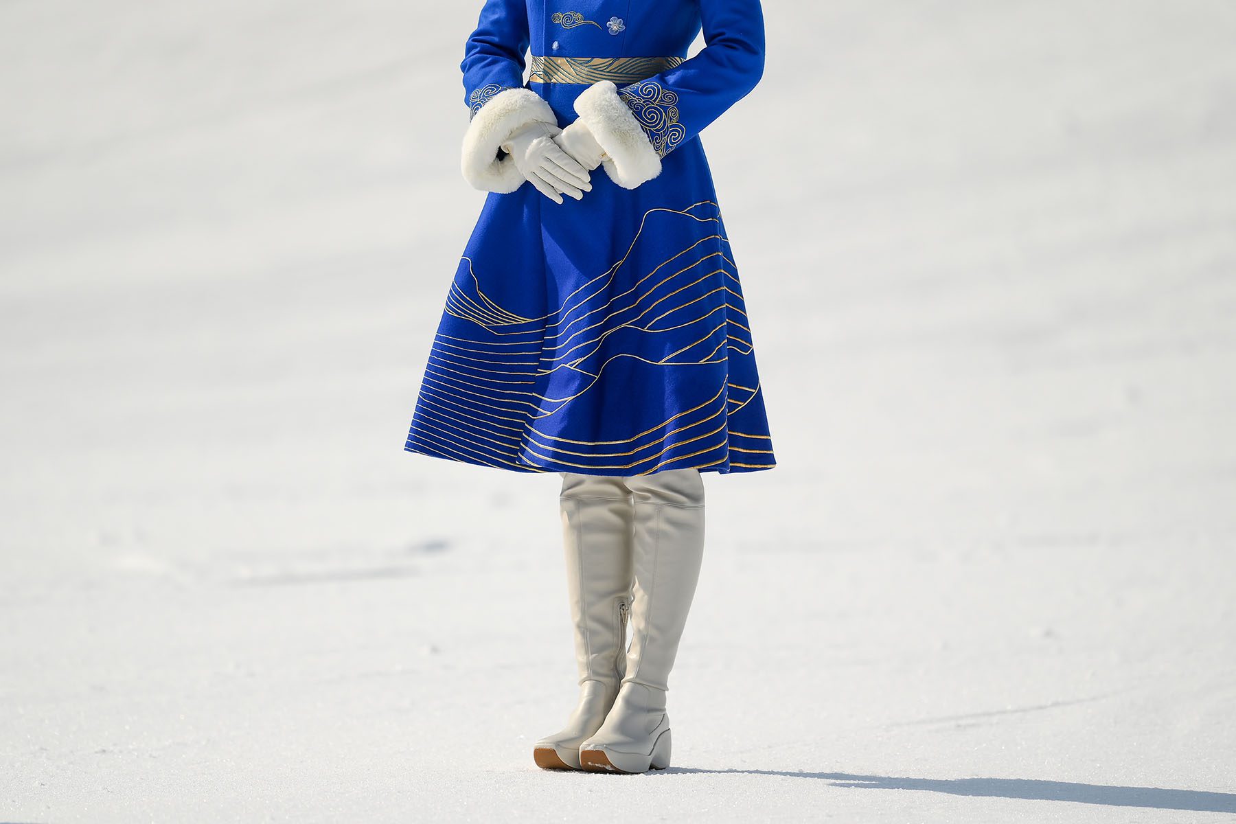 A hostess wearing a blue dress and white boots stands during a ceremony.