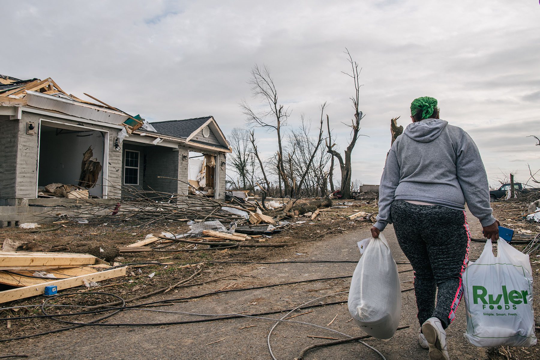 A woman carries shopping bags as she walks by homes destroyed by a tornato.
