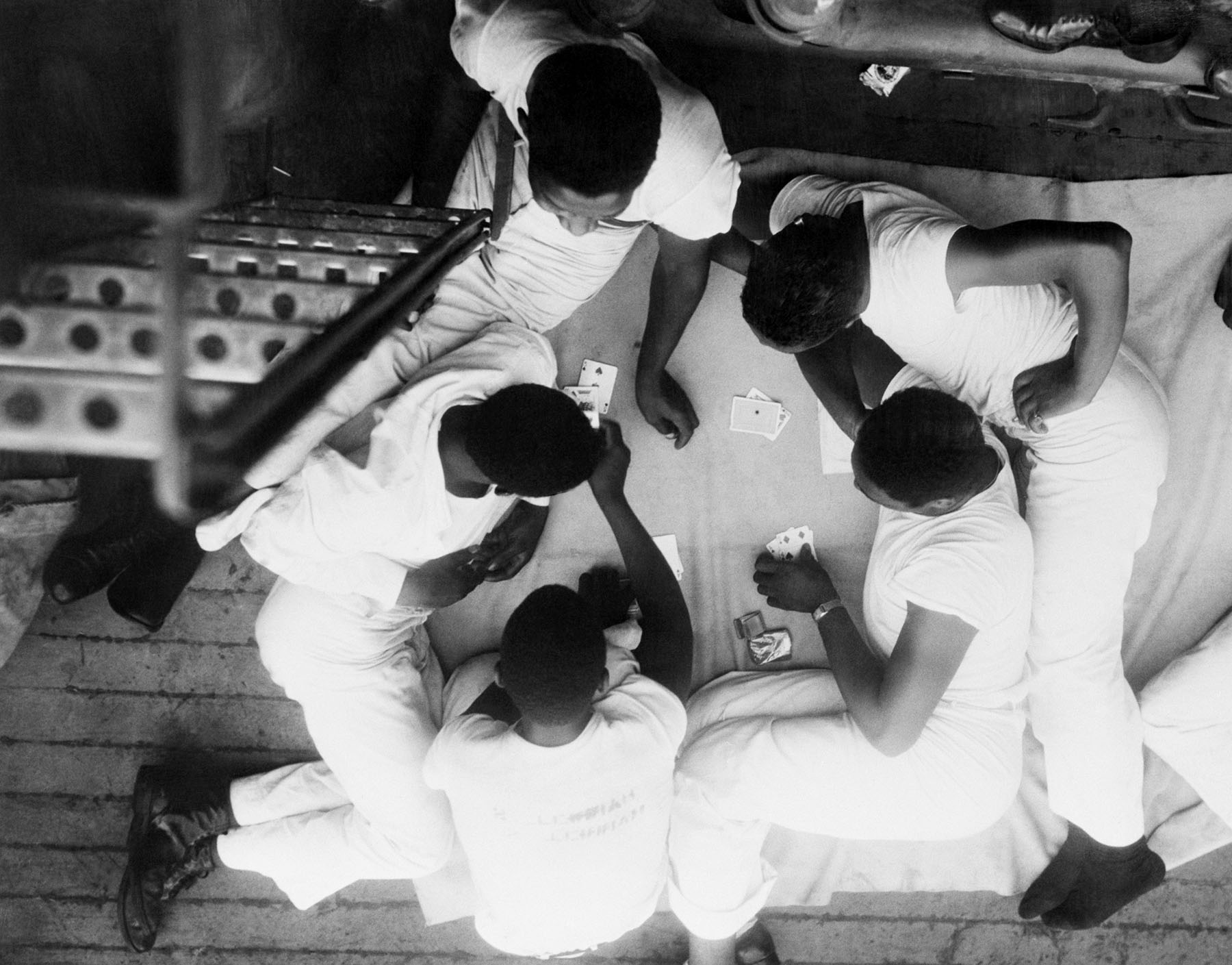 Young men sit in a circle playing cards aboard a Navy ship.