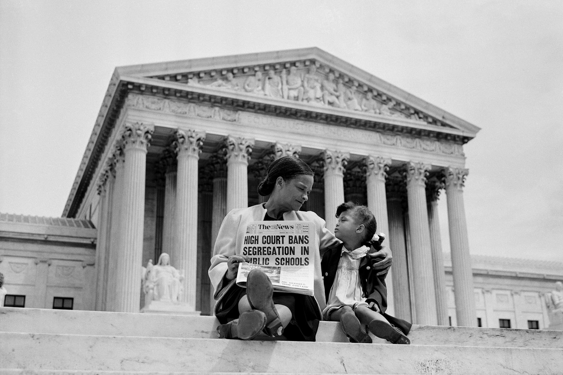 Nettie Hunt and her daughter Nickie sit in front of the U.S. Supreme Court as Nettie holds a newspaper that reads "High Court Bans Segregation in Public Schools"