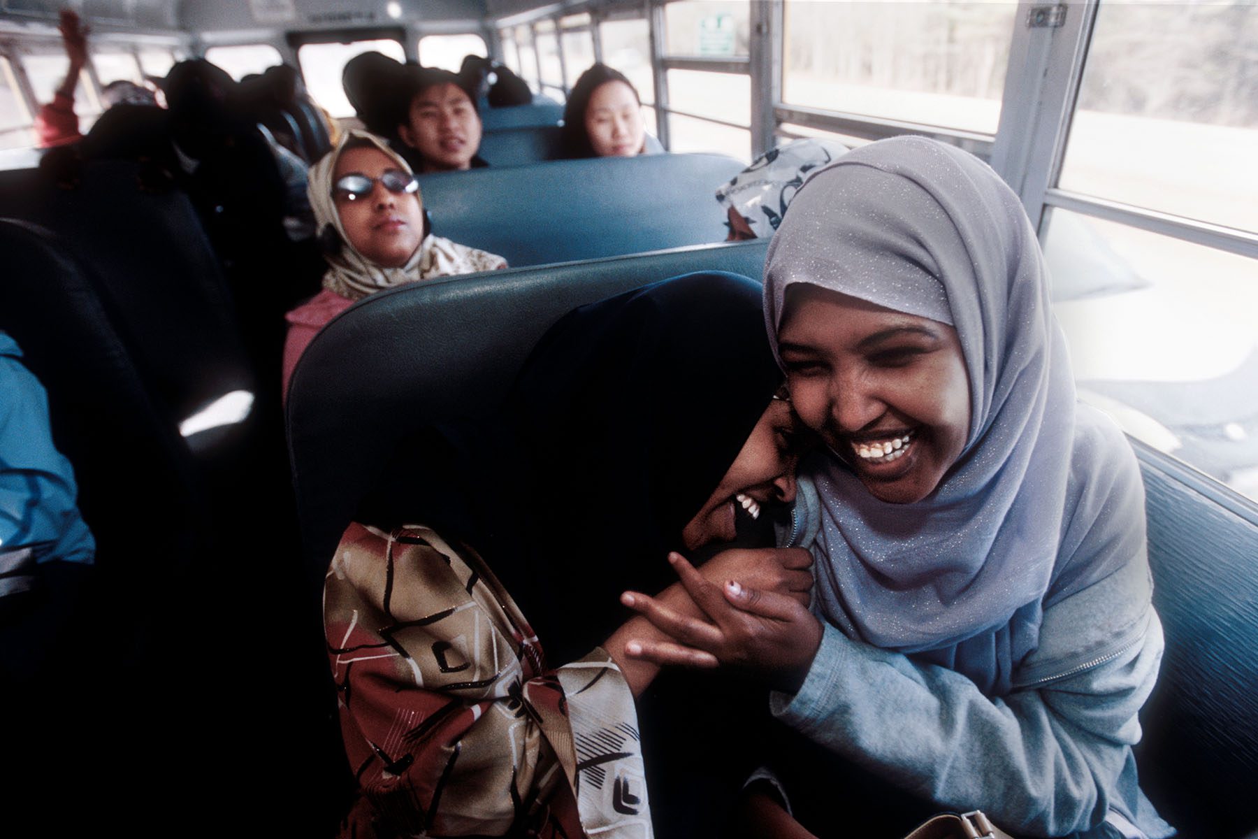 Two veiled students share a laugh in a school bus.