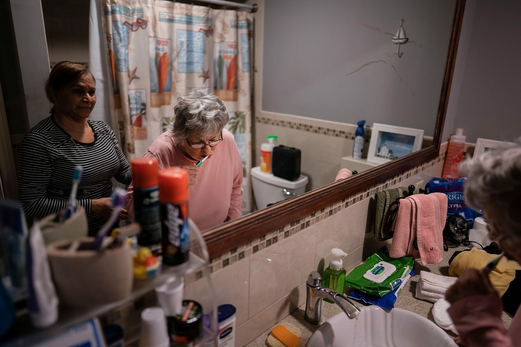 A woman is helped by her caregiver as she brushes her teeth.