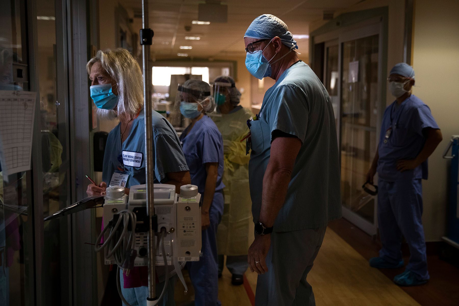 Nurses check on a critically ill patient through a glass door.