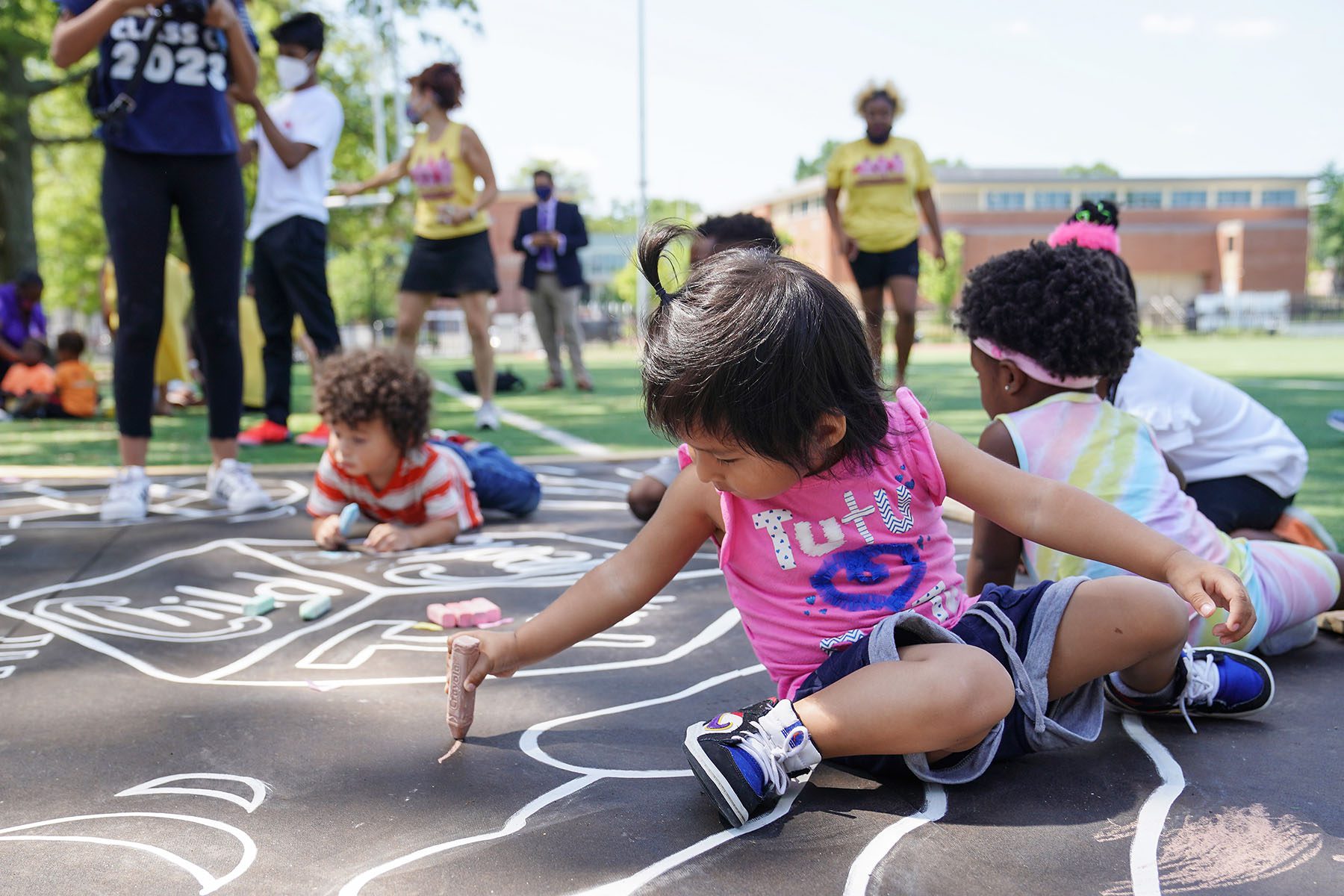 Children use sidewalk chalk to draw a mural on a playground.