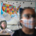 Third grade students wearing masks and using plastic dividers take part in a lesson.