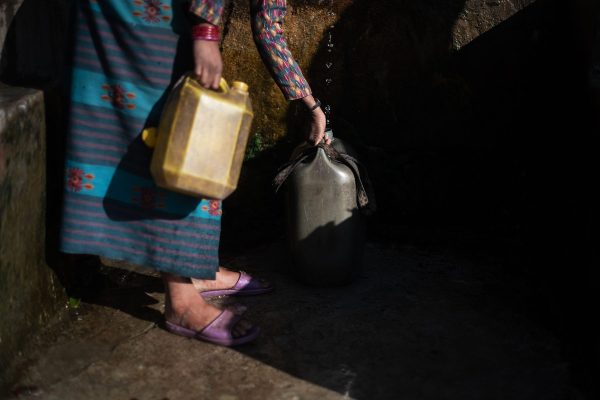 A woman collects water from a source into containers.