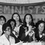 Surrounded by women, Coretta Scott King speaks at a podium during the National Women's Conference