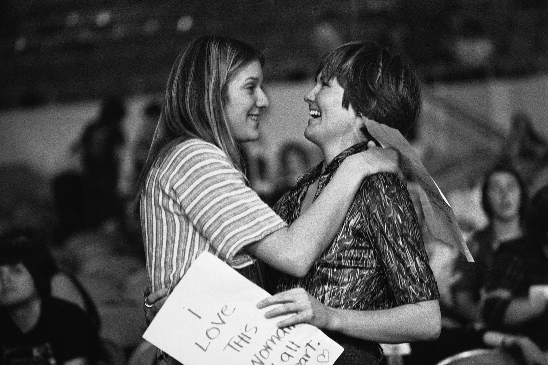 Two women hug each other as they celebrate the passing of the Sexual Preference Resolution. One holds a sign that reads "I Love This Woman."