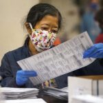 Woman wearing a mask and blue gloves examines a ballot