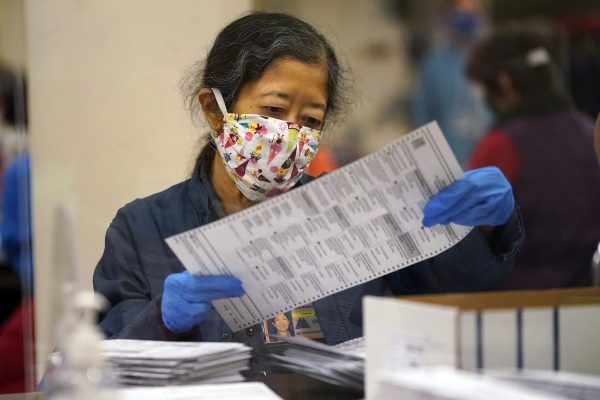 Woman wearing a mask and blue gloves examines a ballot