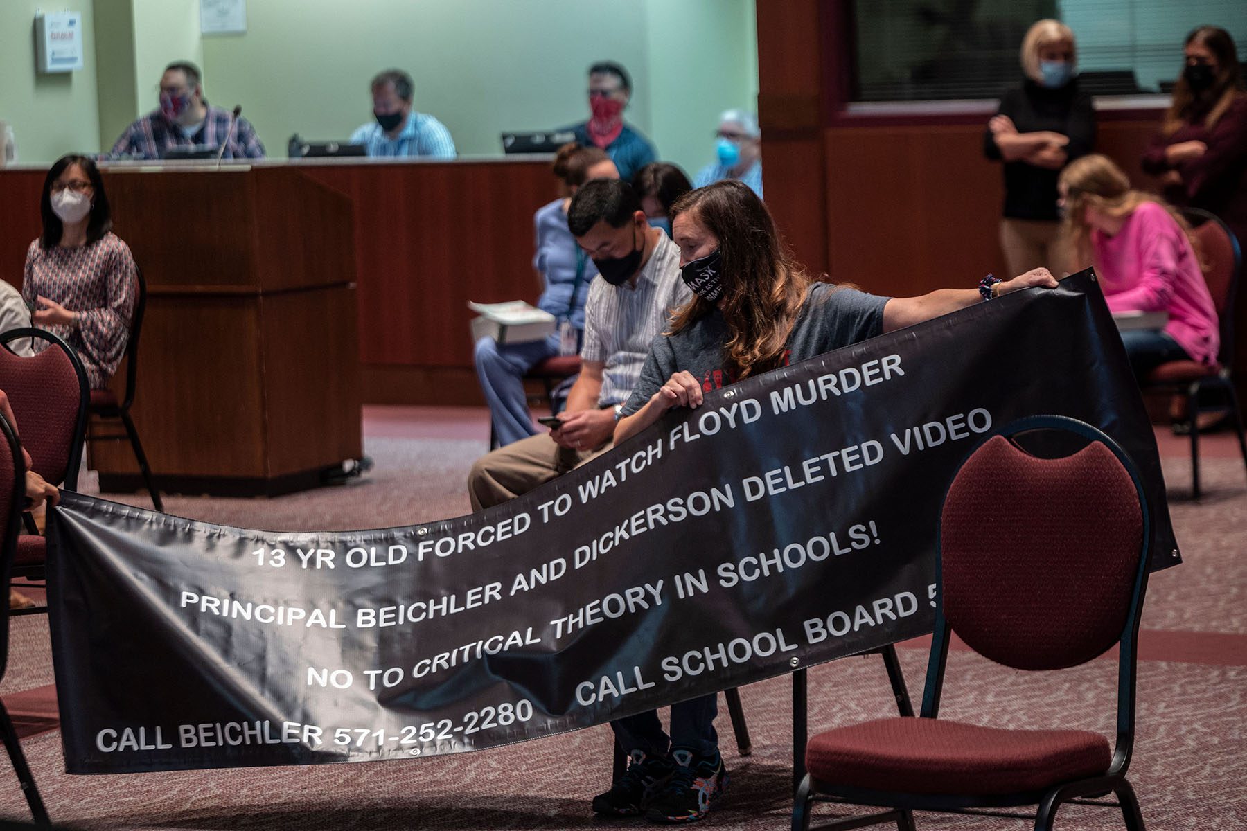 A woman holds up a sign that reads "13 year old forced to watch Floyd murder. Principal Beichler and Dickerson deleted video. No to critical theory in schools!"