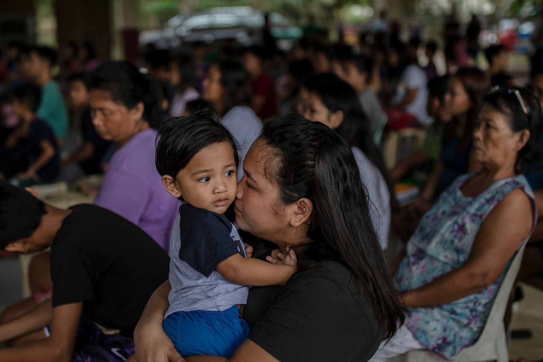A woman surrounded by people at an evacuation center embraces her young son.